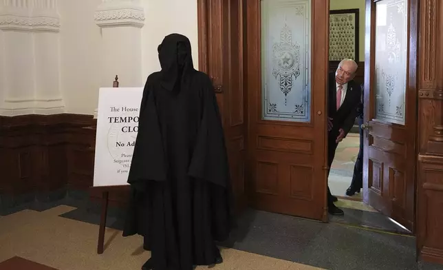 Texas state Sen. Juan "Chuy" Hinojosa, right, looks at a protester dressed as death standing outside of the House Chamber where Democratic Texas state Rep. Nicole Collier refuses to leave due to a required law enforcement escort, Tuesday, Aug. 19, 2025, in Austin, Texas. (AP Photo/Eric Gay)