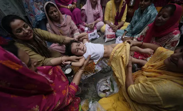 Hindu women belonging to the Dogra community swing a child as part of a ritual as they pray for the long life of their sons during Bacch Dua festival in Jammu, India, Tuesday, Aug.19, 2025.(AP Photo/Channi Anand)