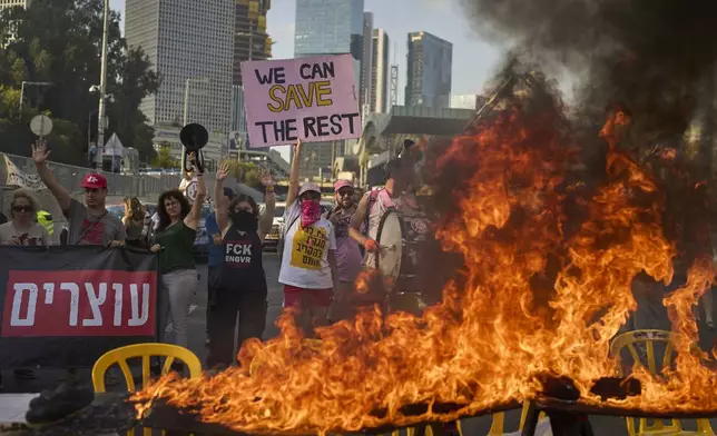 Demonstrators block a highway and burn an installation of a Shabbat dinner table demanding the immediate release of hostages held by Hamas and calling for the Israeli government to reverse its decision to take over Gaza City and other areas in the Gaza Strip, in Tel Aviv, Israel, Friday, Aug. 22, 2025. (AP Photo/Ohad Zwigenberg)