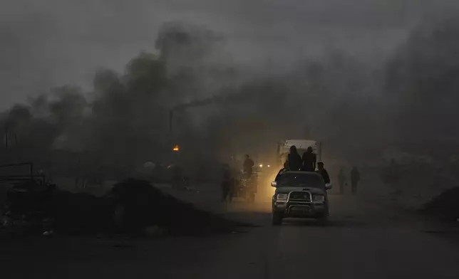 Palestinians ride their vehicles through black smoke from makeshift burners used to extract fuel from melted plastic along the Sea Road, at dusk in the south of Gaza City, Thursday, Aug. 21, 2025. (AP Photo/Abdel Kareem Hana)