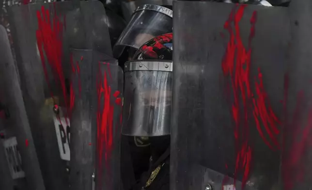 A police officer looks out from shields on which demonstrators smeared paint at a protest against the war in Gaza, in Mexico City, Sunday, Aug. 17, 2025. (AP Photo/Fernando Llano)