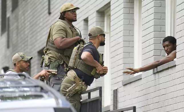 Armed officers prepare to place handcuffs on a man from within an apartment complex, Tuesday, Aug. 19, 2025, in the Petworth neighborhood of northwest Washington. The officers pictured had "Washington Field Office" on their shirts underneath tactical gear that said Police. (AP Photo/Jacquelyn Martin)