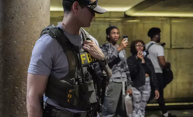 An FBI agent stands by as District of Columbia Metro Transit Police Department and Metropolitan Police Department officers detain three people at L'Enfant Plaza metro station, Thursday, Aug. 21, 2025, in Washington. (AP Photo/Julia Demaree Nikhinson)