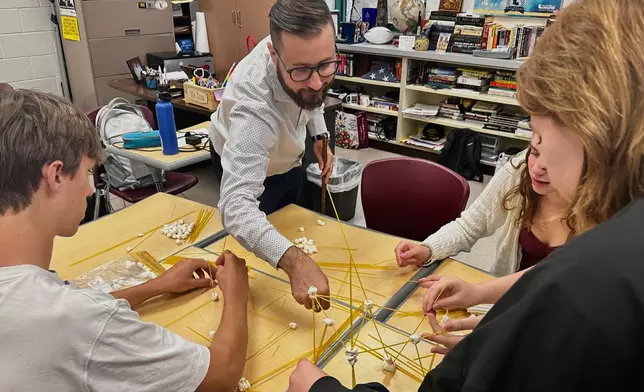 Benjamin Franklin High School teacher Chris Dier helps students create a structure made of pasta and marshmallows, as an ice breaker on the second day of classes on Aug. 12, 2025, in New Orleans. (AP Photo/Stephen Smith)
