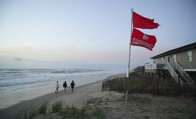 Three women walk the beach at sunrise as waves from Hurricane Erin crash ashore in Nags Head, N.C., on Wednesday, Aug. 20, 2025. (AP Photo/Allen G. Breed)
