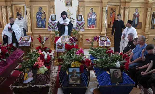 CAPTION CORRECTS THE SPELLING - Mourners at the funeral of Natalia Haiova, her sons Vladyslav and Roman, and her brother Oleksandr, who were killed in their apartment in Kyiv during the Russian strike on July 31, in Ivankovychi, Kyiv region, Ukraine, Tuesday, Aug. 5, 2025. (AP Photo/Danylo Antoniuk)