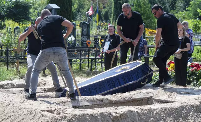 CAPTION CORRECTS THE SPELLING - Cemetery workers are seen lowering a casket into the grave during a funeral of Natalia Haiova, her sons Vladyslav and Roman, and her brother Oleksandr, who were killed in their apartment in Kyiv during the Russian strike on July 31, in Ivankovychi, Kyiv region, Ukraine, Tuesday, Aug. 5, 2025. (AP Photo/Danylo Antoniuk)