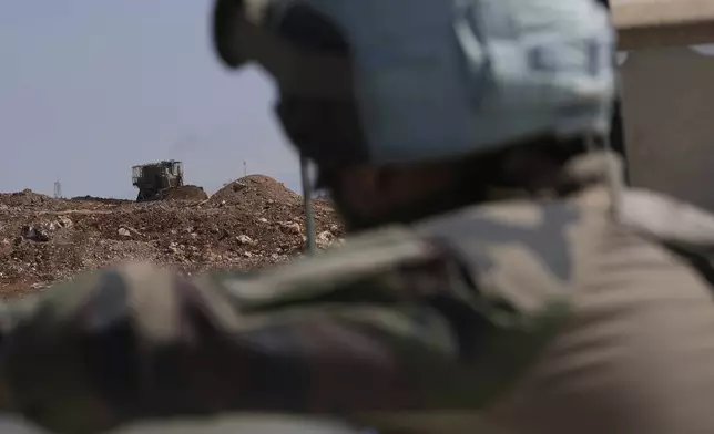 A French U.N. peacekeeper, foreground, watches an Israeli bulldozer building a sand barrier at one of five new Israeli army positions along the road between Houla and Kfar Kila, southern Lebanon, Wednesday, Aug. 20, 2025, following airstrikes and a ground offensive that destroyed nearby villages. (AP Photo/Hussein Malla)