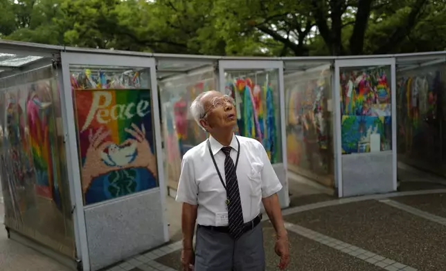 Kunihio Iida, atomic bomb survivor and a volunteer guide speaks in English to foreign visitors looks app the sky in front of the Children's Peace Monument where the place where people offer paper cranes to honor the victims of the 1945 atomic bomb on Wednesday, July 9, 2025, in Hiroshima, western Japan. (AP Photo/Eugene Hoshiko)