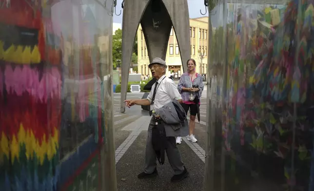Kunihio Iida, atomic bomb survivor and a volunteer guide speaks in English to foreign visitors in front of the Children's Peace Monument where the place where people offer paper cranes to honor the victims of the 1945 atomic bomb on Wednesday, July 9, 2025, in Hiroshima, western Japan. (AP Photo/Eugene Hoshiko)