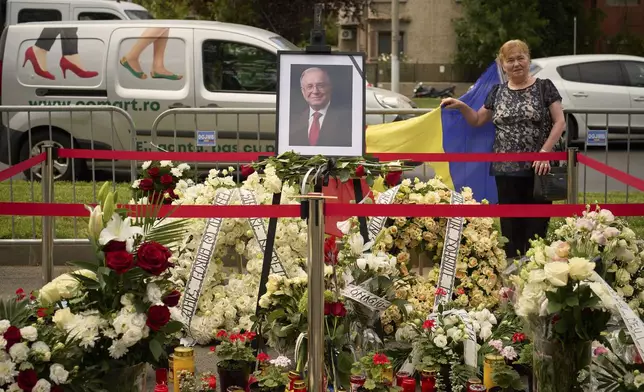 A woman poses next to floral tributes for the late Ion Iliescu, Romania's first freely elected president after the fall of communism in 1989, outside the Cotroceni Presidential Palace, in Bucharest, Romania, Wednesday, Aug. 6, 2025.(AP Photo/Vadim Ghirda)