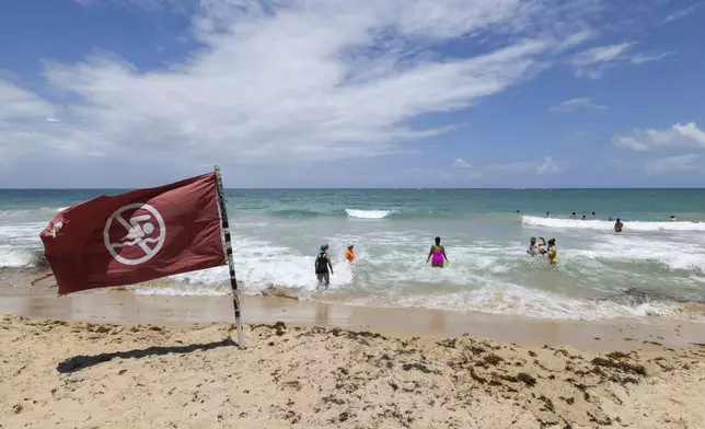 A warning flag flies on the beach as people swim in Condado, Puerto Rico, as Hurricane Erin approaches, Friday, Aug. 15, 2025. (AP Photo/Alejandro Granadillo)