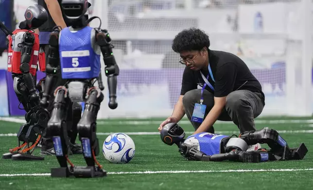 A technician assists a robot that fell during a soccer match at the World Humanoid Robot Games in Beijing, China, Friday, Aug. 15, 2025. (AP Photo/Mahesh Kumar A.)