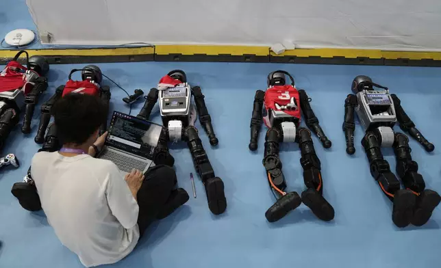 A technicians works on robots during the World Humanoid Robot Games in Beijing, China, Friday, Aug. 15, 2025. (AP Photo/Mahesh Kumar A.)