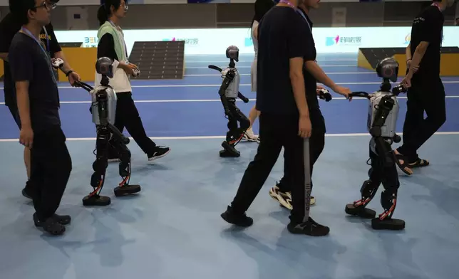Technicians guide robots away after they competed in a soccer event at the World Humanoid Robot Games Beijing, China, Saturday, Aug. 16, 2025. (AP Photo/Mahesh Kumar A.)