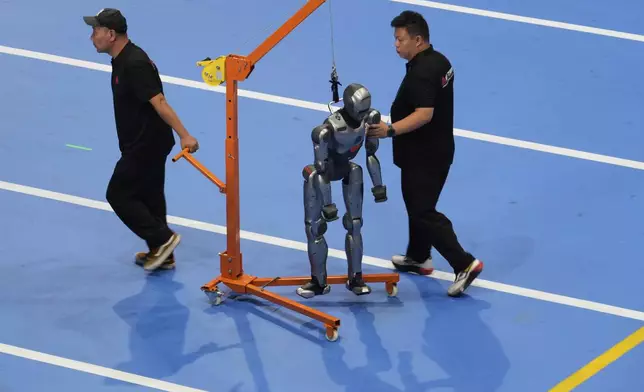 Workers transfer a robot before the opening ceremony for the World Humanoid Robot Games held in Beijing, China, Thursday, Aug. 14, 2025. (AP Photo/Mahesh Kumar A.)