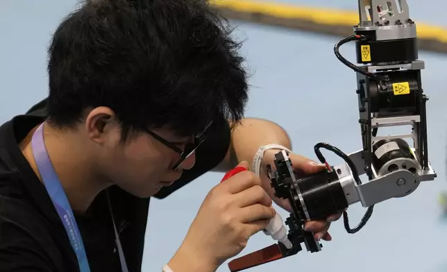 A technician fixes the arm of a robot during the World Humanoid Robot Games held in Beijing, China, Saturday, Aug. 16, 2025. (AP Photo/Mahesh Kumar A.)