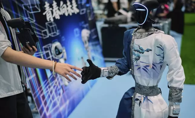 A woman touches the hand of a robot that performed in the dance event at the World Humanoid Robot Games Beijing, China, Saturday, Aug. 16, 2025. (AP Photo/Mahesh Kumar A.)