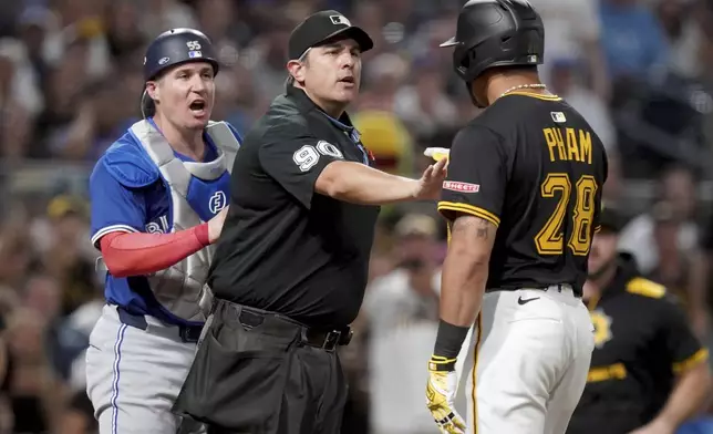 Home plate umpire Mark Ripperger, center, gets between Toronto Blue Jays catcher Tyler Heineman, left, and Pittsburgh Pirates' Tommy Pham, right, during the seventh inning of a baseball game Monday, Aug. 18, 2025, in Pittsburgh. (AP Photo/Matt Freed)