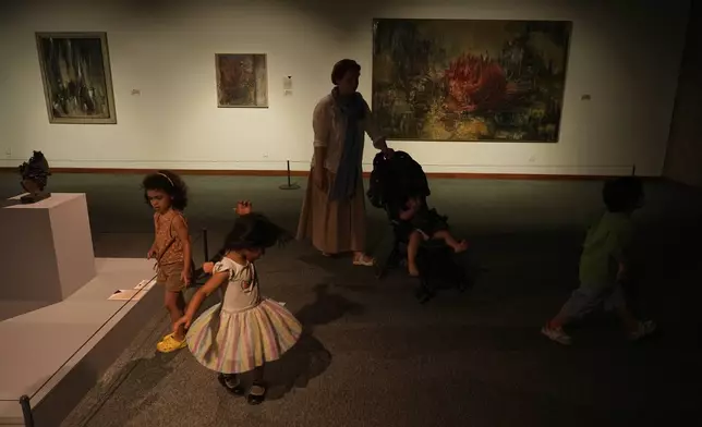 A woman pushes a stroller as children play while visiting an exhibition called "In Women's Words" showing some artworks of modern Iranian women artists from the collection of the Tehran Museum of Contemporary Art, Iran, Sunday, Aug. 3, 2025. (AP Photo/Vahid Salemi)
