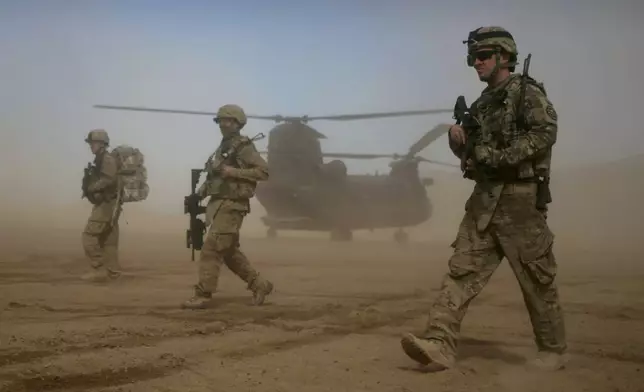 FILE - U.S. soldiers, part of the NATO- led International Security Assistance Force (ISAF), walk as a U.S. Chinook helicopter is seen on the back ground in Shindand, Herat, west of Kabul, Afghanistan, Jan. 28, 2012. (AP Photo/Hoshang Hashimi, File)