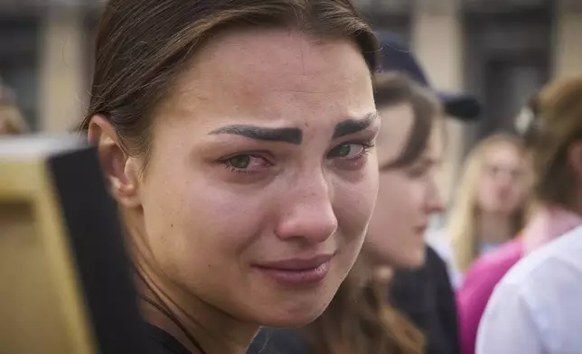 A colleague cries as she looks at a portrait of Victoria Roshchyna, 27, a Ukrainian journalist who reported on the Russian invasion of Ukraine and died in Russian captivity, during the funeral ceremony in the Independence square in central Kyiv, Ukraine, Friday, Aug. 8, 2025. (AP Photo/Efrem Lukatsky)