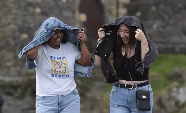 Giselle Munoz Alarcon, left, and Dominica Sepulveda Gutierrez shield from the wind at Carrickfergus Castle, Co Antrim, Northern Ireland, Monday Aug. 4, 2025, as weather warnings are coming into force with Storm Floris expected to cause severe travel disruption to road, air and ferry services, and close bridges. (Liam McBurney/PA via AP)
