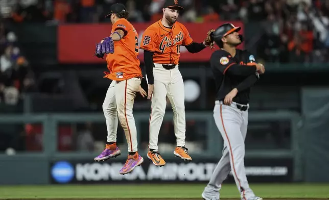 San Francisco Giants shortstop Willy Adames, left, and second baseman Casey Schmitt celebrate the team's victory as Baltimore Orioles' Luis Vázquez, foreground, walks off the field after a baseball game, Friday, Aug. 29, 2025, in San Francisco. (AP Photo/Godofredo A. Vásquez)