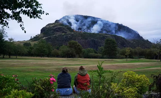 Members of the public watch the smoke and flames from a fire on Arthur's Seat in Holyrood Park, in Edinburgh, Scotland, Sunday, Aug. 10, 2025. (Jane Barlow/PA via AP)