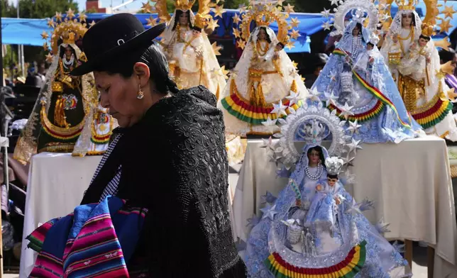 A woman walks by a display of statues depicting the Virgin of Copacabana, Bolivia's patroness, before the start of a procession in her honor, in Copacabana, Bolivia, Tuesday, Aug. 5, 2025. (AP Photo/Juan Karita)