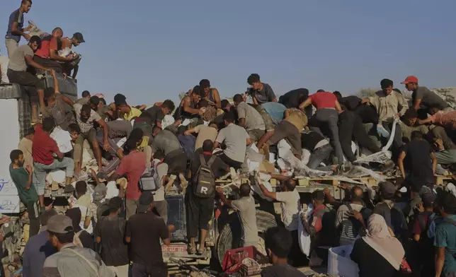 Palestinians struggle to get food and humanitarian aid from the back of a truck as it moves along the Morag corridor near Rafah, in the southern Gaza Strip, Monday, Aug. 4, 2025. (AP Photo/Mariam Dagga)