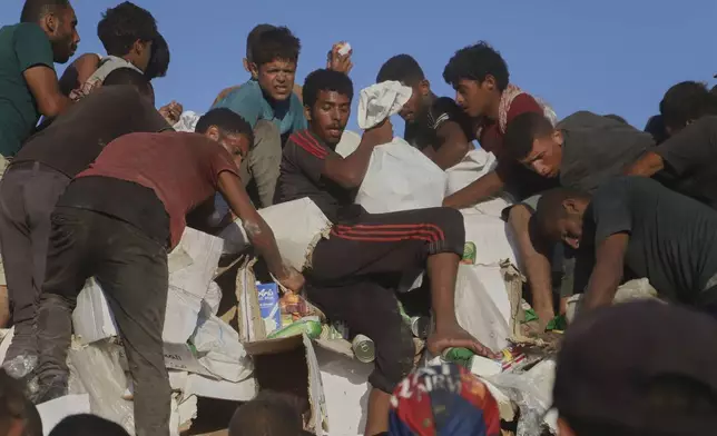 Palestinians struggle to get food and humanitarian aid from the back of a truck as it moves along the Morag corridor near Rafah, in the southern Gaza Strip, Monday, Aug. 4, 2025. (AP Photo/Mariam Dagga)