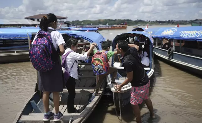 Salvador Mitidieri helps schoolchildren board his boat after classes in Santa Rosa, Peru, Monday, Aug. 18, 2025. (AP Photo/Ivan Valencia)