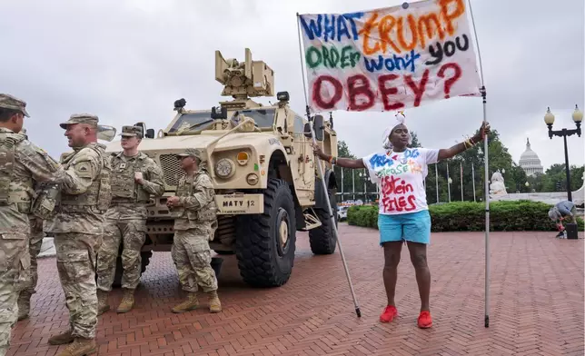 Nadine Seiler of Waldorf, Md., displays her banner as protesters, police, and National Guard troops congregate at the entrance to Union Station in Washington, Wednesday, Aug. 20, 2025. (AP Photo/J. Scott Applewhite)