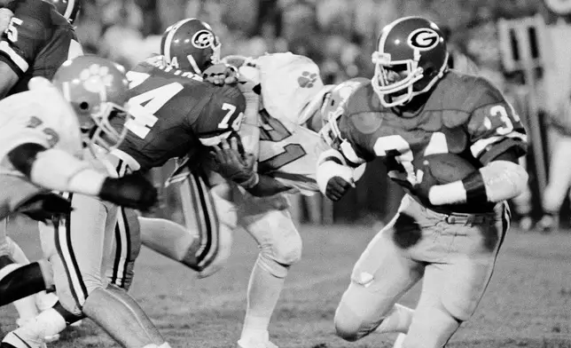 FILE - Georgia's Herschel Walker (34) goes around Clemson's Dan Benish (71) with some help from Georgia's Guy McIntyre (74) during third period of an NCAA college football game Monday night, Sept. 6, 1982 in Athens, Ga. (AP Photo/Charles Kelly, File)