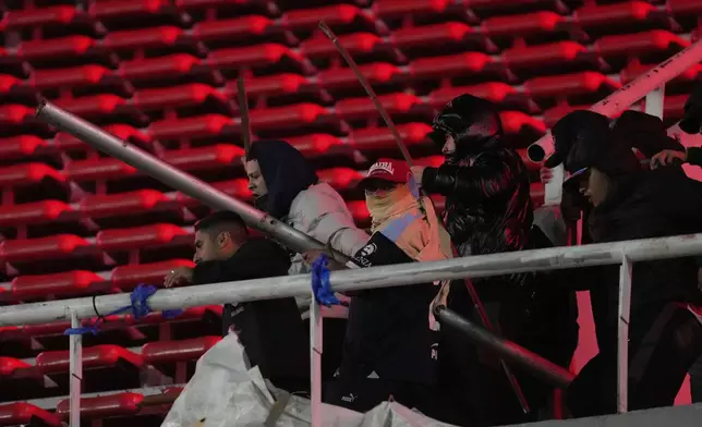 Fans of Argentina's Independiente hold metal bars during clashes with Universidad de Chile fans after a Copa Sudamericana round of sixteen second leg soccer match was suspended at the Libertadores de America stadium in Avellaneda, Argentina, Wednesday, Aug. 20, 2025. (AP Photo/Gustavo Garello)