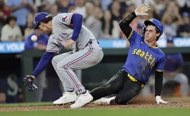 Seattle Mariners' Cole Young scores on a passed ball as Texas Rangers pitcher Jacob Latz reaches for the ball in a baseball game Thursday, July 31, 2025, in Seattle. (AP Photo/John Froschauer)