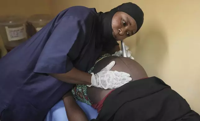 A midwife checks a pregnant woman at a facility run by aid group International Rescue Committee, in Magumeri, in northeast Nigeria's Borno state, Tuesday, July 22, 2025. (AP Photo/Sunday Alamba)