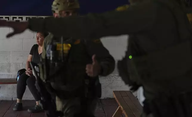 A woman watches as immigration agents conduct an operation at a car wash on Friday, Aug. 15, 2025, in Montebello, Calif. (AP Photo/Gregory Bull)