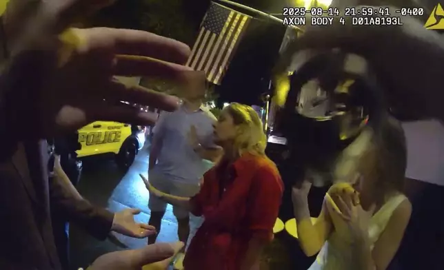 In an image taken from police body camera footage, a Newport Police officer pulls handcuffs into view to arrest Rhode Island Special Assistant Attorney General Devon Flanagan, in red, after restaurant representatives indicated that they did not want her and her companions on their premises, an encounter that ended with officers detaining Flanagan on trespassing charges, Aug. 14, 2025, in Newport, R.I. (Newport Police Department via AP)