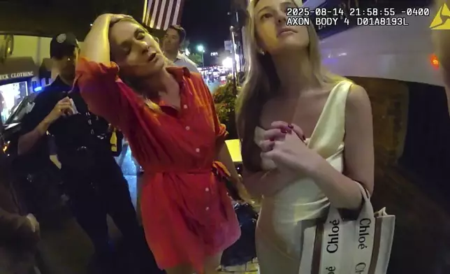 In an image taken from police body camera footage, Newport Police officers interacting with Rhode Island Special Assistant Attorney General Devon Flanagan, in red, and her companions after restaurant representatives indicated that they did not want them on their premises, an encounter that ended with officers detaining Flanagan on trespassing charges, Aug. 14, 2025, in Newport, R.I. (Newport Police Department via AP)