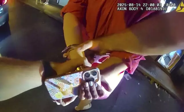 In an image taken from police body camera footage, a Newport Police officer handcuffing Rhode Island Special Assistant Attorney General Devon Flanagan, in red, after an encounter that ended with officers detaining Flanagan on trespassing charges, Aug. 14, 2025, in Newport, R.I. (Newport Police Department via AP)