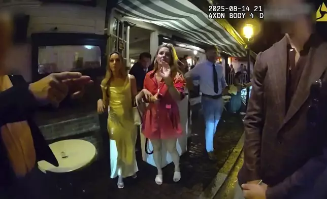 In an image taken from police body camera footage, Newport Police officers interact with Rhode Island Special Assistant Attorney General Devon Flanagan, in red, and her companions after restaurant representatives indicated that they did not want them on their premises, an encounter that ended with officers detaining Flanagan on trespassing charges, Aug. 14, 2025, in Newport, R.I. (Newport Police Department via AP)