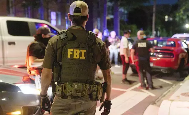 Federal law enforcement agents from various agencies including Bureau of Alcohol, Tobacco, Firearms and Explosives, Park Police, and FBI, question a couple who had been parked outside a legal parking zone while eating McDonald's takeout, Tuesday, Aug. 12, 2025, in northwest Washington near Kennedy St. NW. The couple were released after a search of the car. (AP Photo/Jacquelyn Martin)