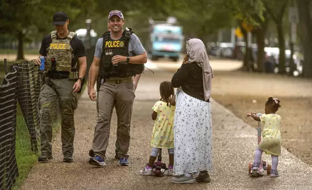 A woman and children watch as officers with the Drug Enforcement Administration patrol along the National Mall Wednesday, Aug. 13, 2025, in Washington. (AP Photo/Mark Schiefelbein)