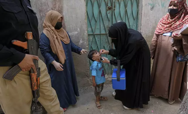 A police officer stands guard while a health worker, center, administers a polio vaccine to a child in Karachi, Pakistan, April 21, 2025. (AP Photo/Fareed Khan)