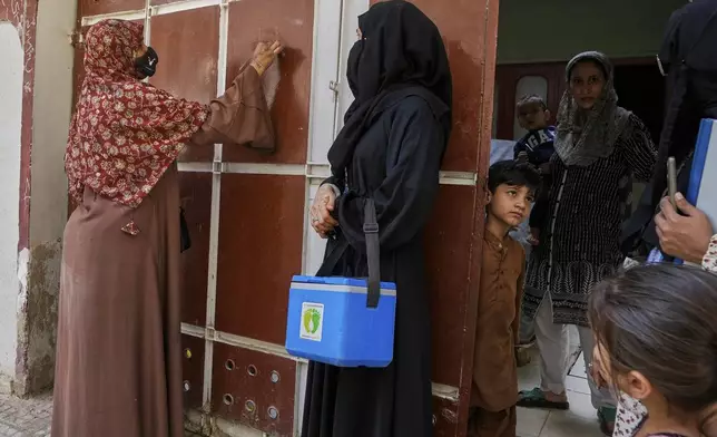 A health worker, left, marks a house after administering polio vaccines in Karachi, Pakistan, April 21, 2025. (AP Photo/Fareed Khan)