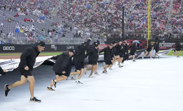 Members of the grounds crew pull up the tarp for the start of the MLB Speedway Classic baseball game between the Atlanta Braves and the Cincinnati Reds at Bristol Motor Speedway in Bristol, Tenn., Saturday, Aug. 2, 2025. (AP Photo/Chris Carlson)