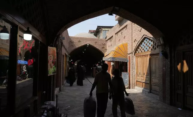 People carry their shopping at the historic neighborhood of Oudlajan in Tehran, Iran, Thursday, July 31, 2025. (AP Photo/Vahid Salemi)