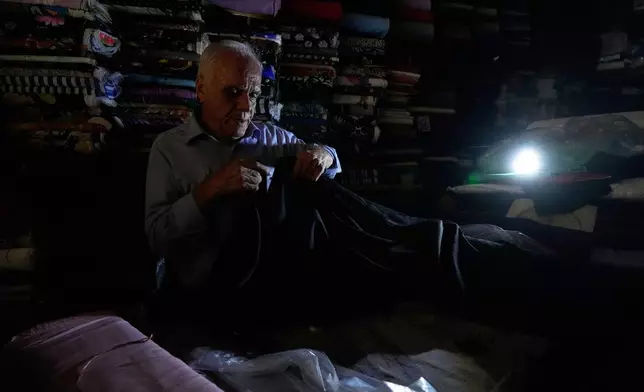 A textile seller works at his shop during power outage in Tehran, Iran, Tuesday, Aug. 5, 2025. (AP Photo/Vahid Salemi)